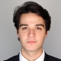 A young man with dark hair and brown eyes wearing a dark suit and white shirt, looking forward with a neutral expression.